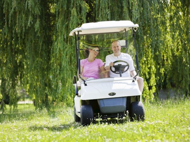 Mann und Frau fahren mit einem E-Cart über eine Wiese